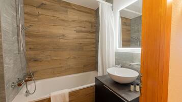 Een moderne badkamer met een houten wand, een witte badkuip, een grote wastafel en een douchehoek.
