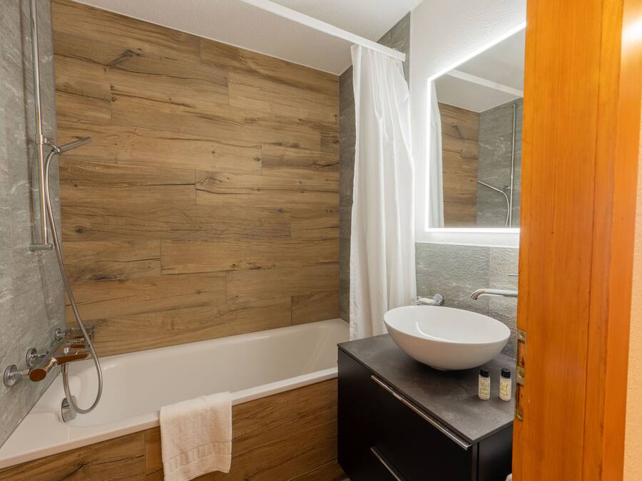 Een moderne badkamer met een houten wand, een witte badkuip, een grote wastafel en een douchehoek.