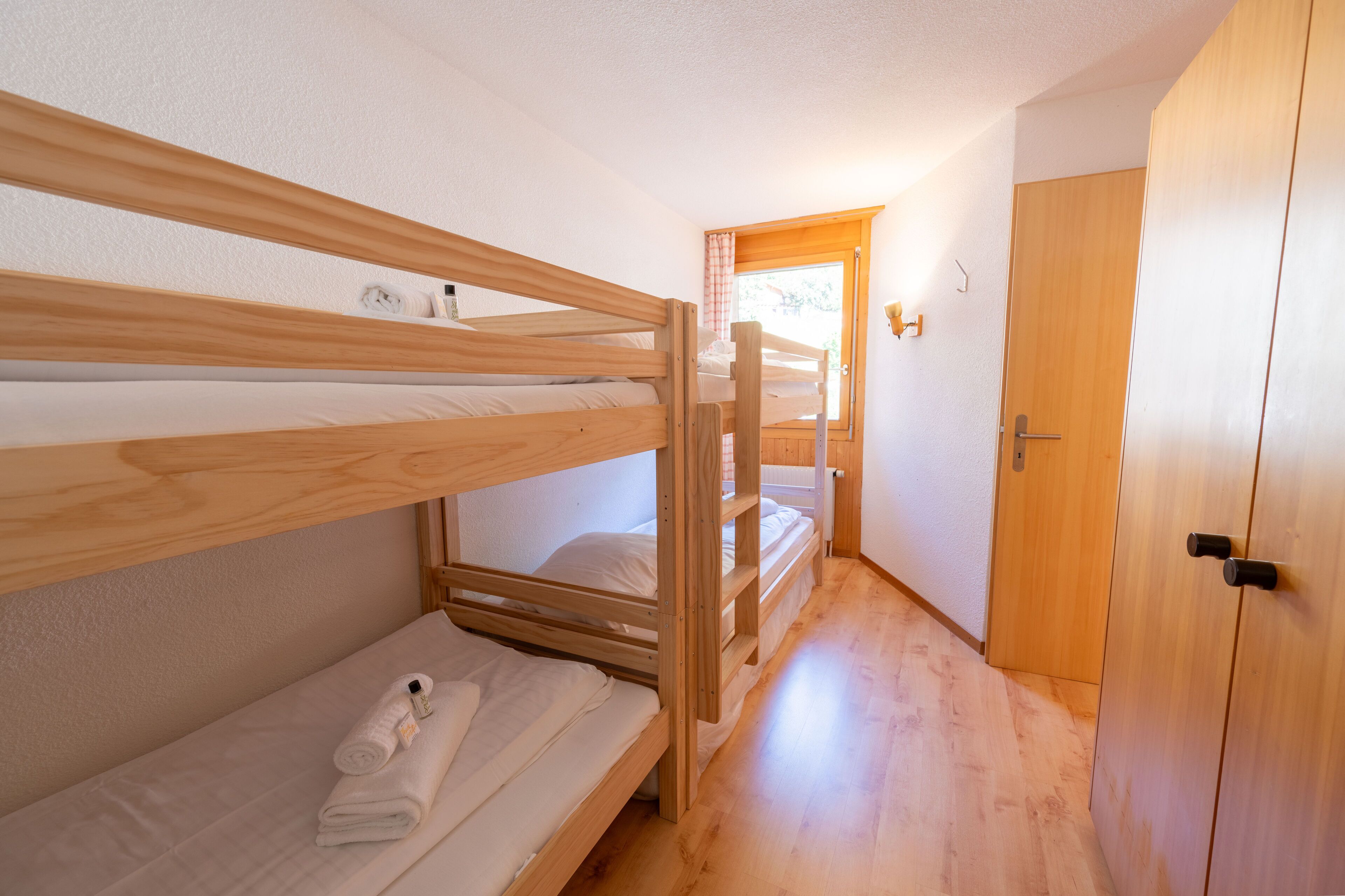Une pièce avec deux lits superposés, une armoire en bois et une porte donnant sur une autre pièce.