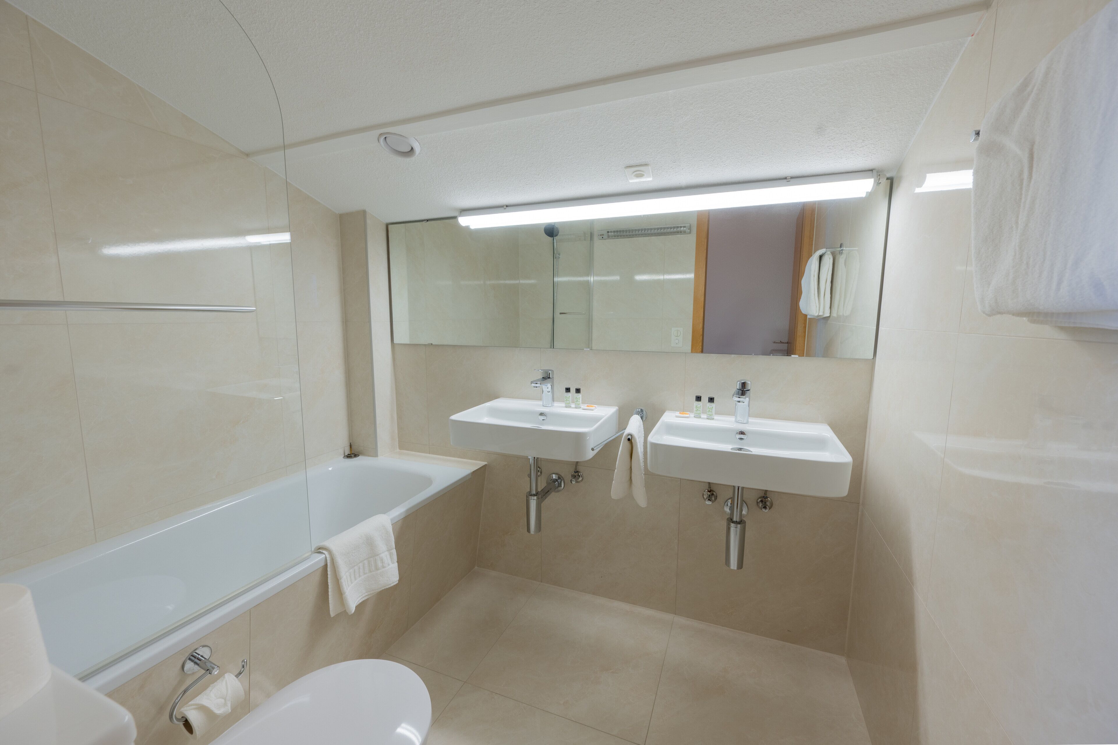 Un baño moderno con bañera, dos lavamanos, inodoro y un espejo grande.