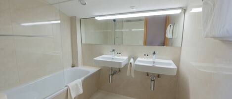 Un baño moderno con bañera, dos lavamanos, inodoro y un espejo grande.