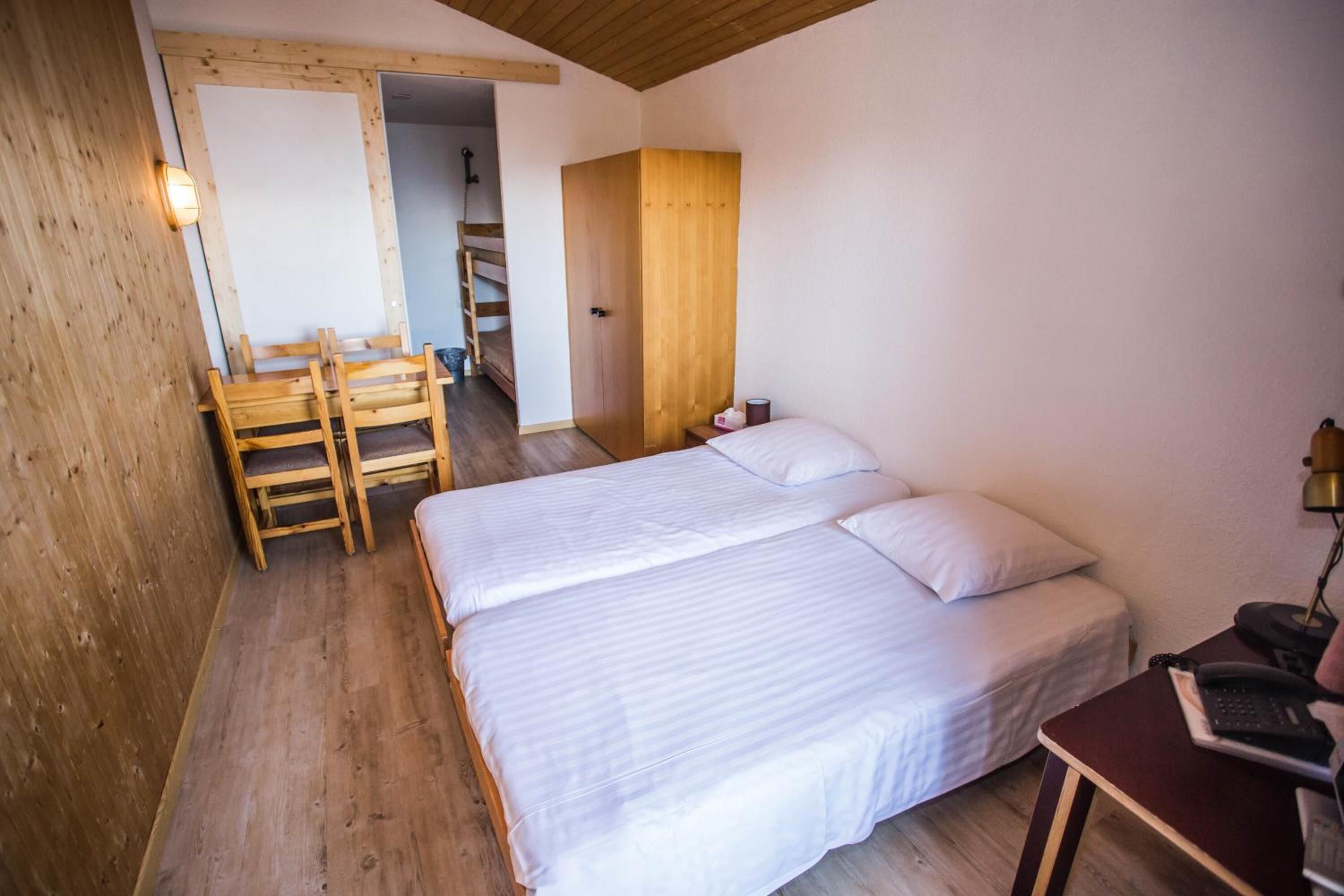 A bedroom with two beds, a wooden desk, a chair, and a wardrobe.