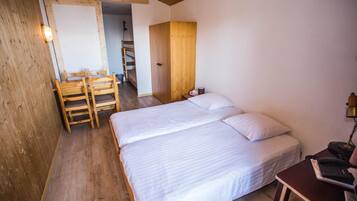 A bedroom with two beds, a wooden desk, a chair, and a wardrobe.
