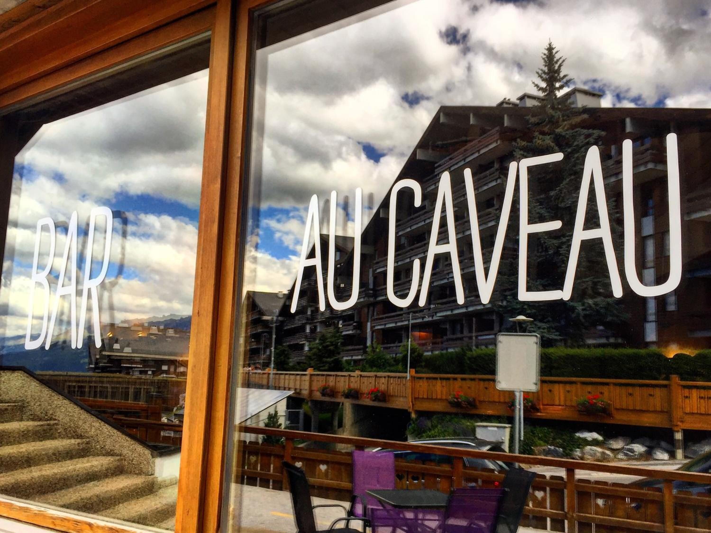 A bar named "BAR AU CAVEAU" with outdoor seating and a view of a mountainous landscape.