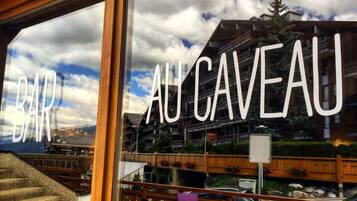A bar named "BAR AU CAVEAU" with outdoor seating and a view of a mountainous landscape.
