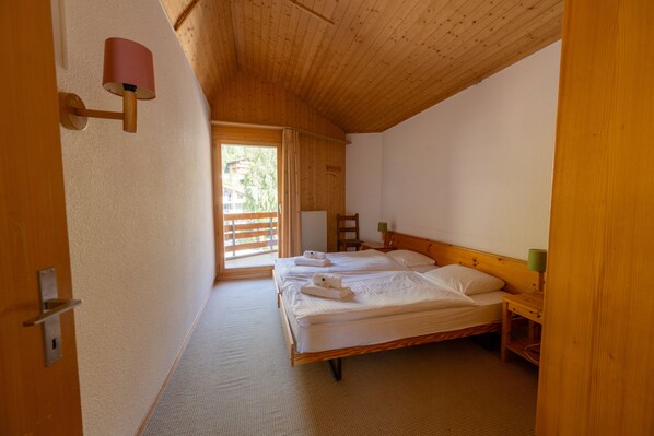 A bedroom with two beds, wooden ceiling, and a view of the outdoors.