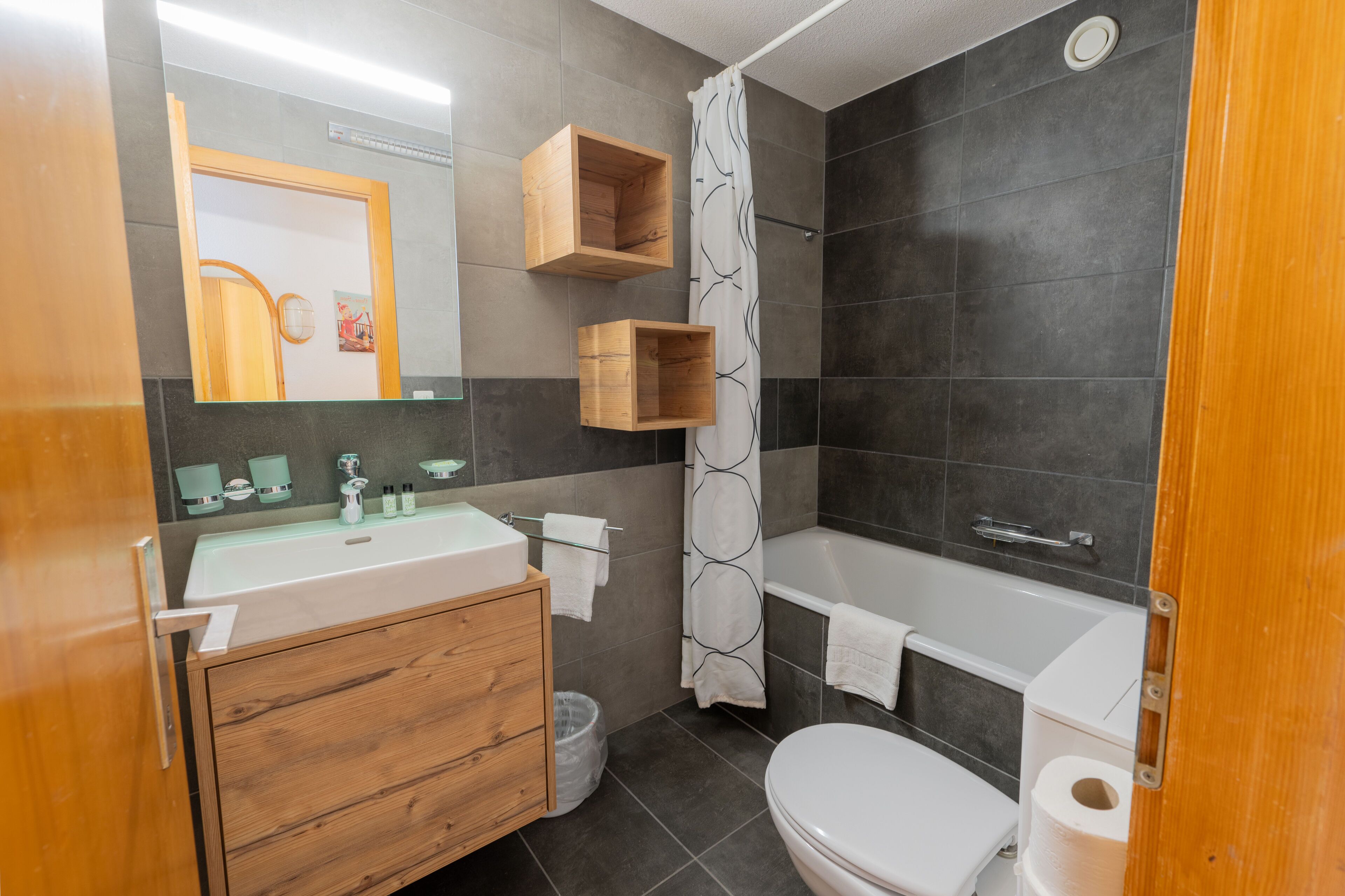 A modern bathroom with a wooden vanity, a white sink, a toilet, and a bathtub.