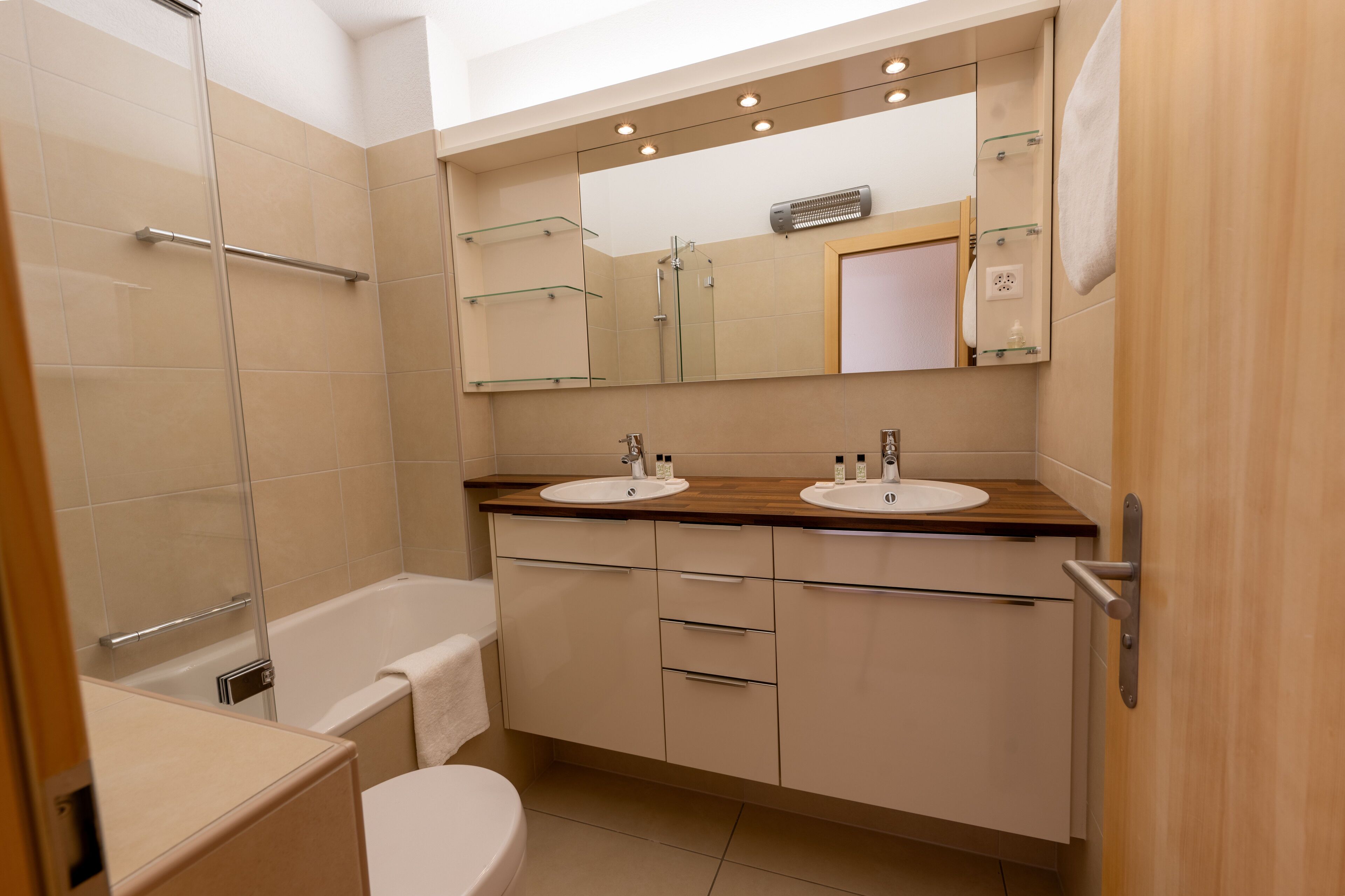 Un baño moderno con dos lavamanos, una bañera y una ducha con mampara de cristal.