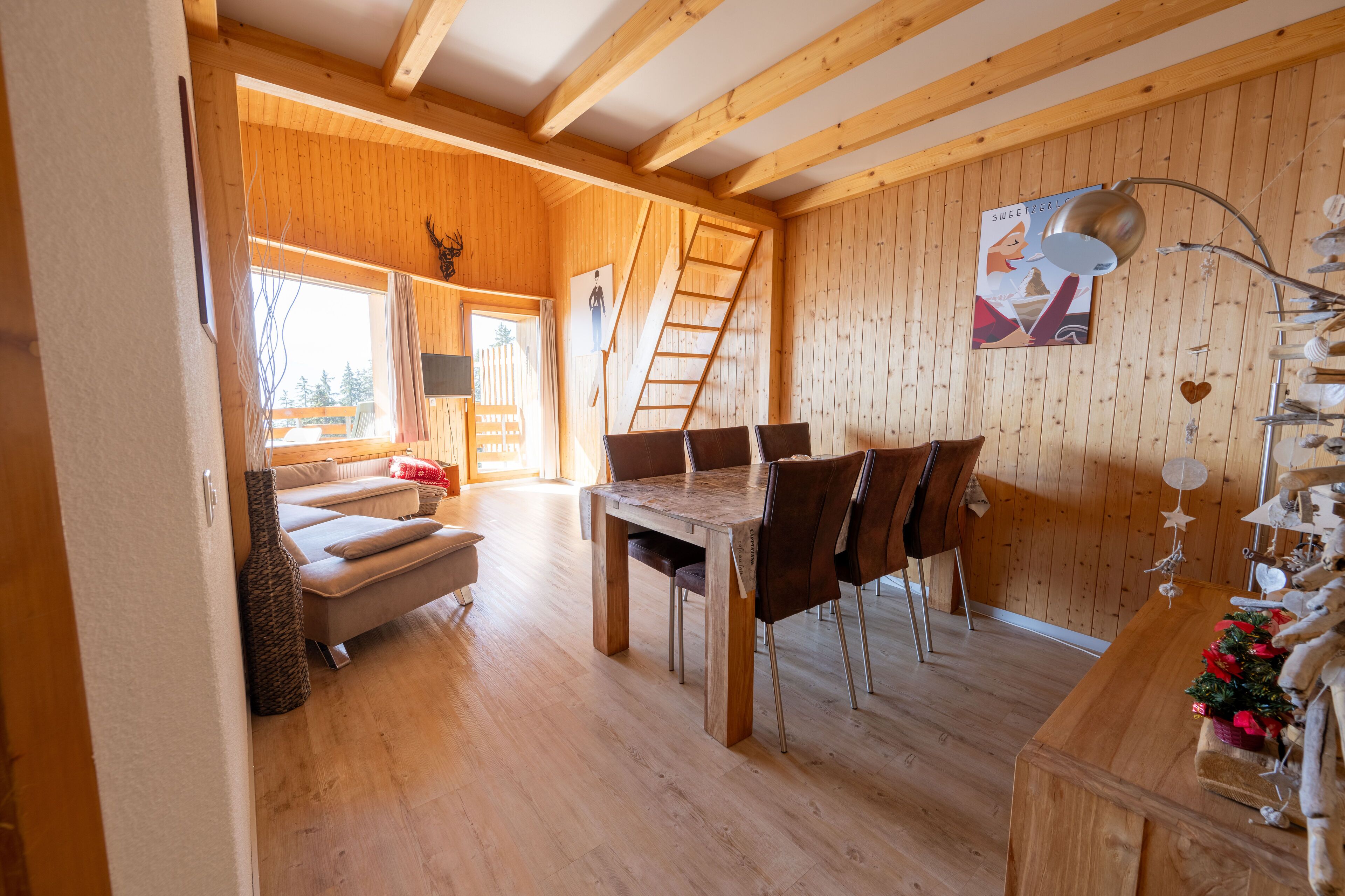 A wooden interior with a dining table and chairs, a sofa, and a ladder against the wall.