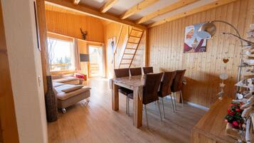 Een houten interieur met een eettafel en stoelen, een bank en een ladder tegen de muur.