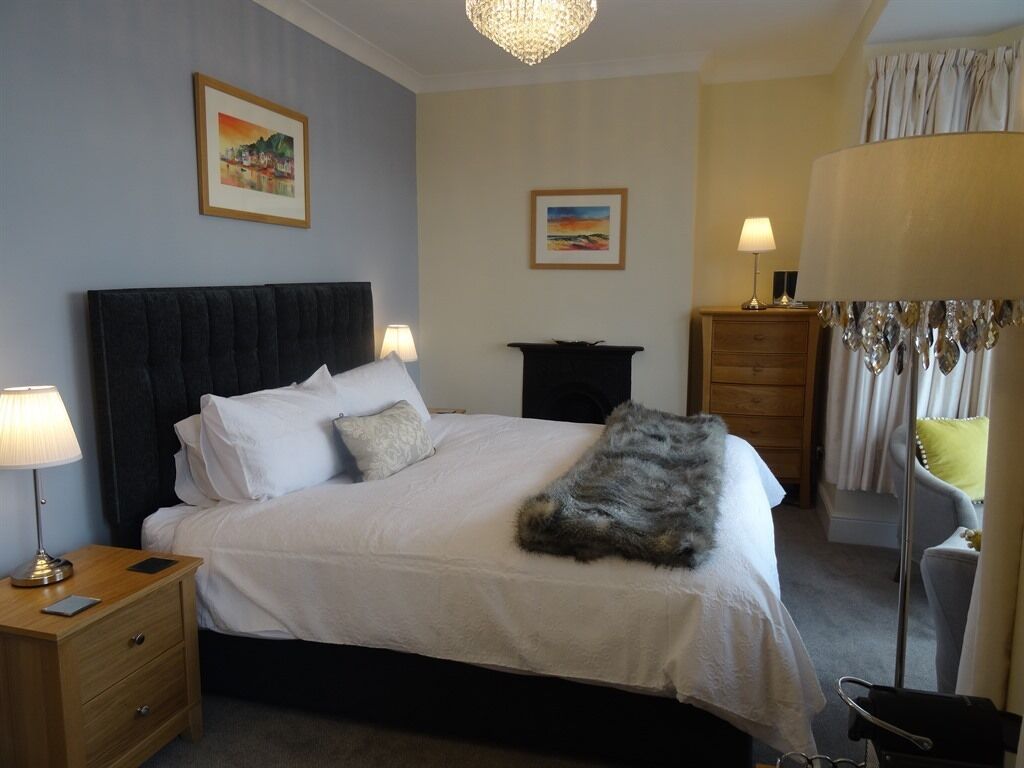 A neatly arranged bedroom with a large bed, bedside lamps, a dresser, and a mirror.