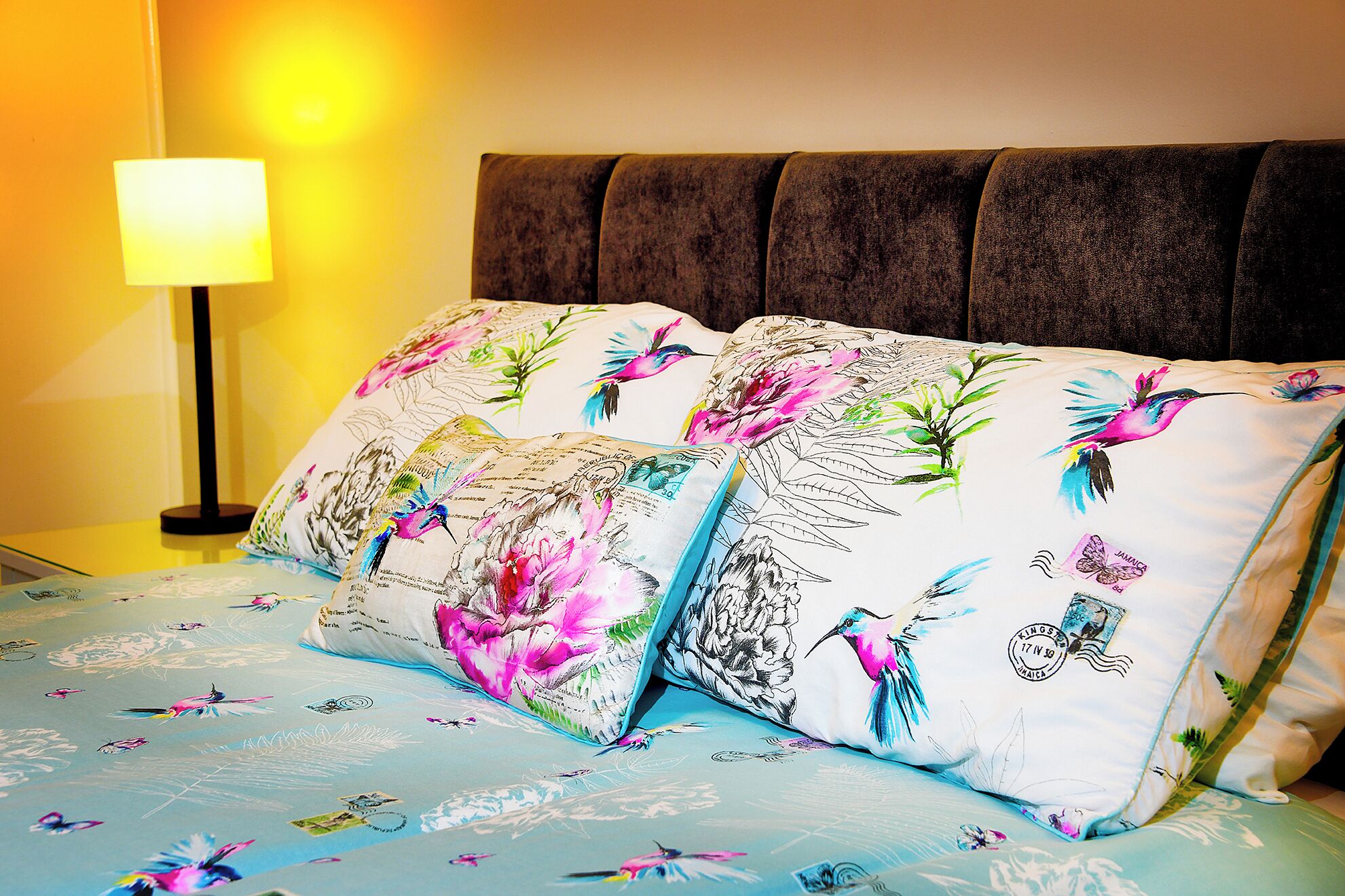 A bed with floral and bird-patterned pillows, a bedside lamp, and a headboard.
