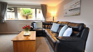 A living room with a black leather sofa, a wooden coffee table, and a potted plant by the window. - Twelve Holiday Apartments (Blackpool)