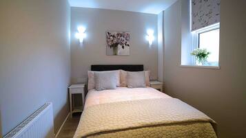 A bedroom with a bed, nightstands, a wall-mounted light, a window with a view, and a radiator.