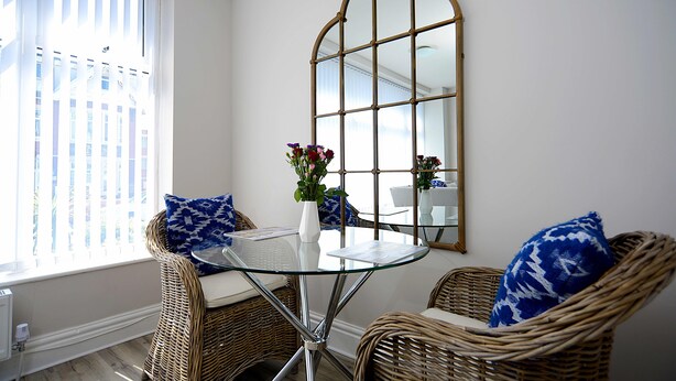 A corner room with wicker furniture, a glass table, and a large mirror. - Twelve Holiday Apartments (Blackpool)