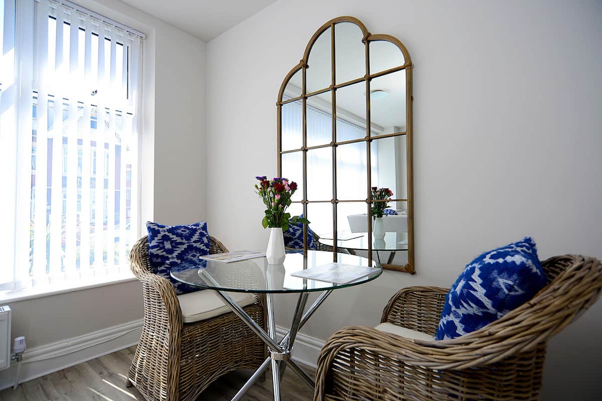 A corner room with wicker furniture, a glass table, and a large mirror.