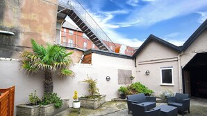A courtyard with outdoor furniture, potted plants, and a staircase leading to an upper level. - Twelve Holiday Apartments (Blackpool)