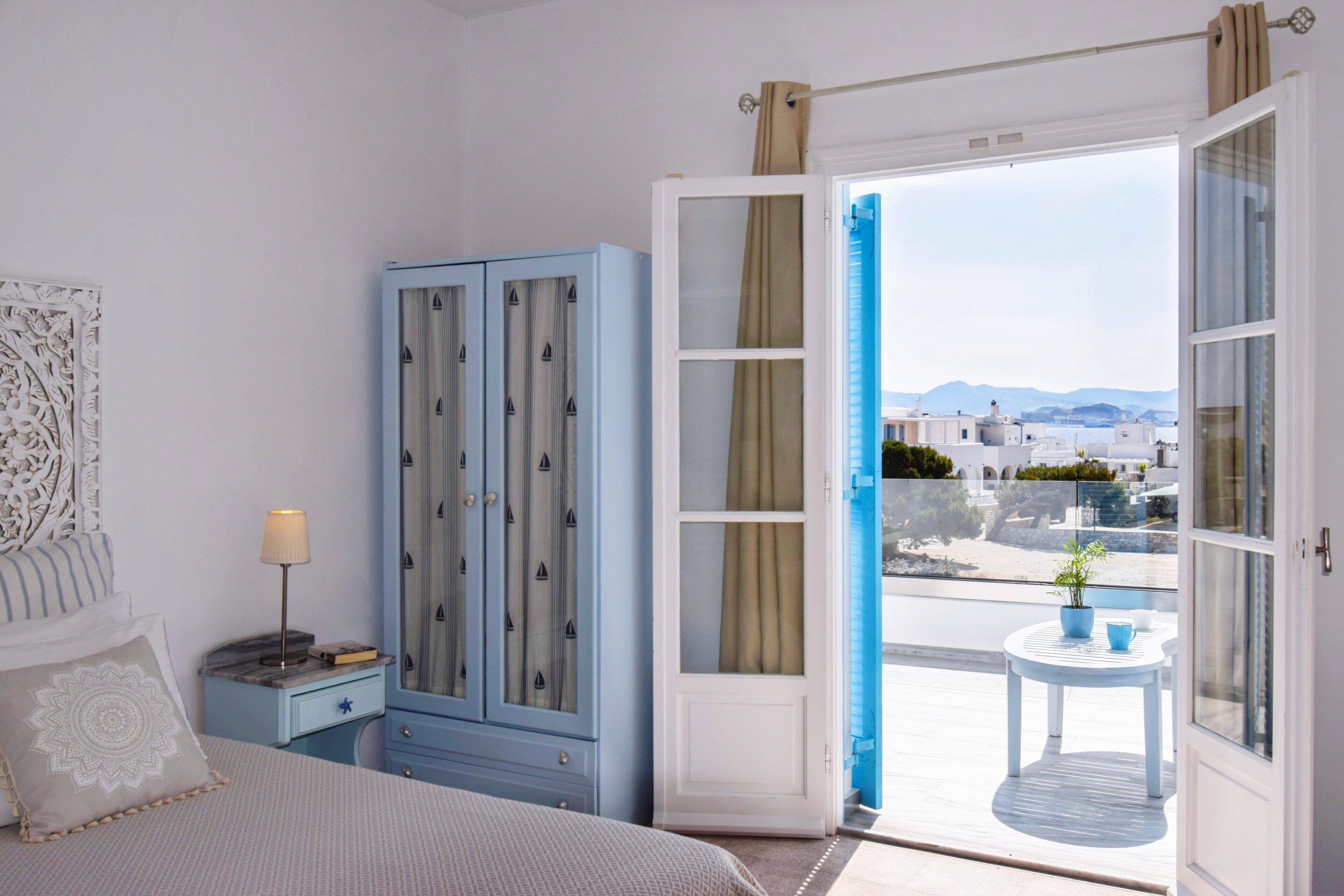 A bedroom with a bed, a nightstand, a wardrobe, and a balcony with a view of buildings and mountains.