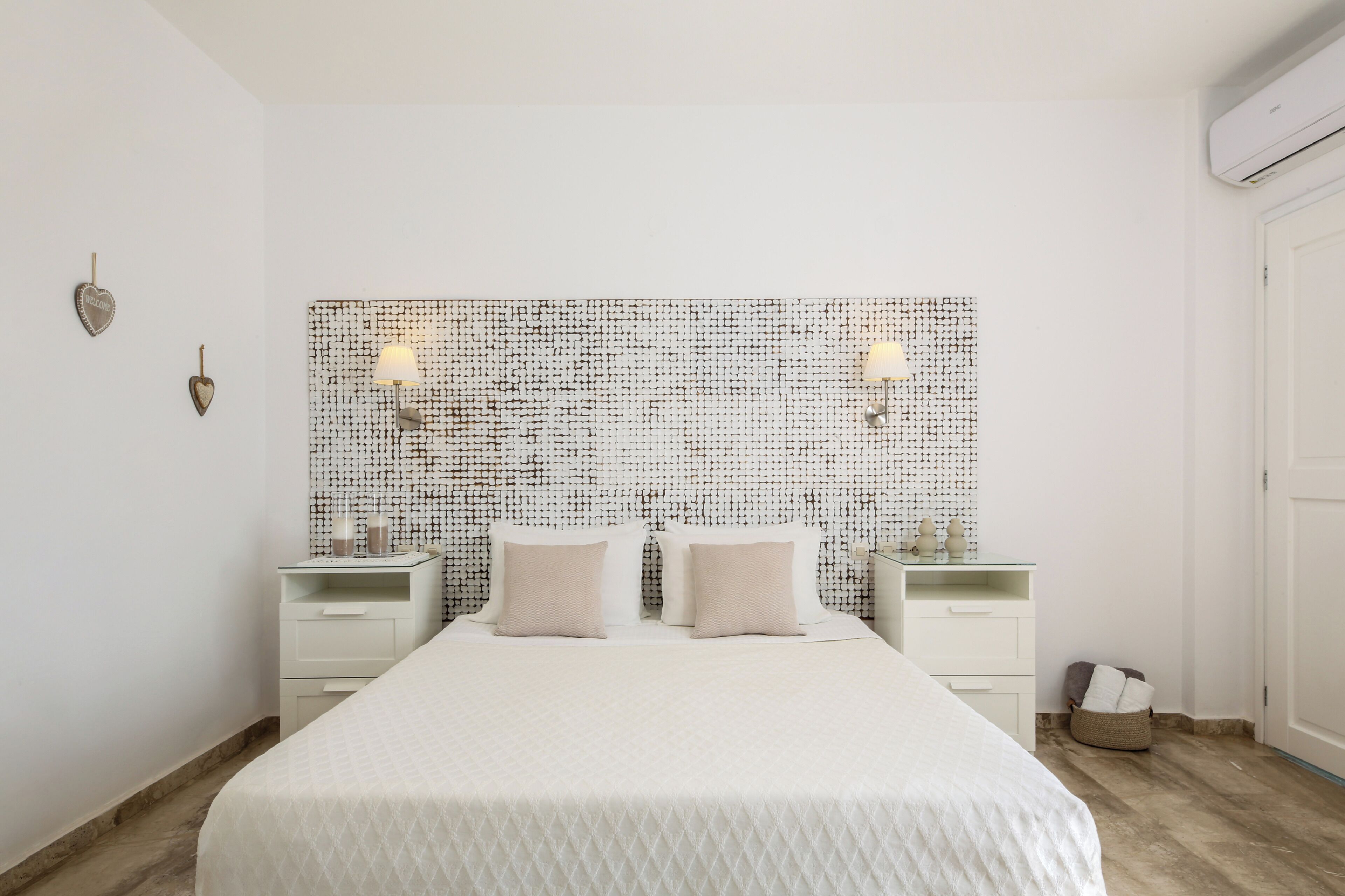 A bedroom with a large bed, two bedside tables, a wall-mounted light fixture, and a small bedside table with a lamp.