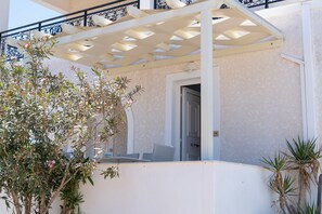 A covered outdoor area with a white pergola, a door, and a small seating area. - Eleana Studios (Paros)