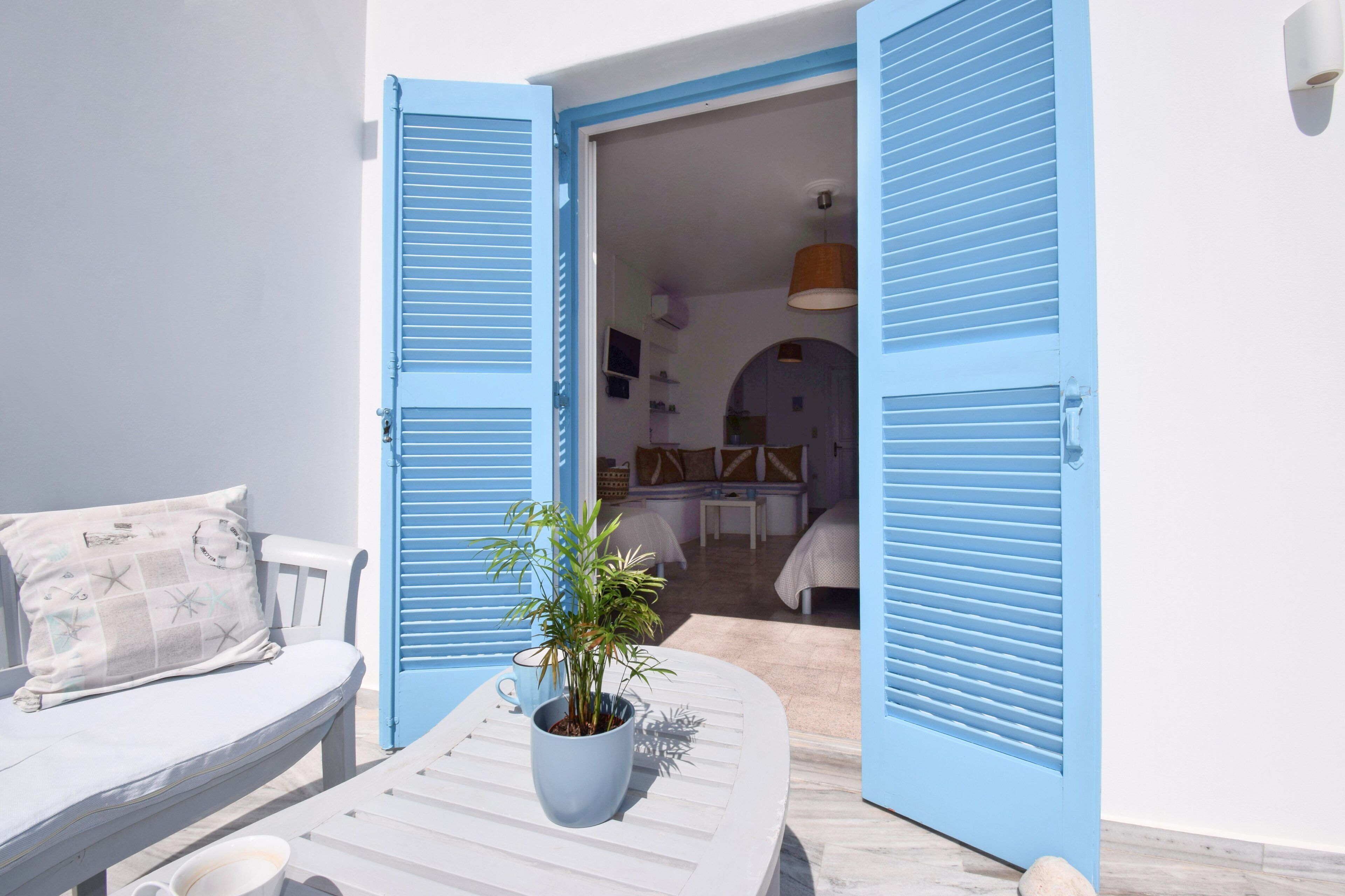 A room with a white bed, a blue potted plant, and a white table with a cup.