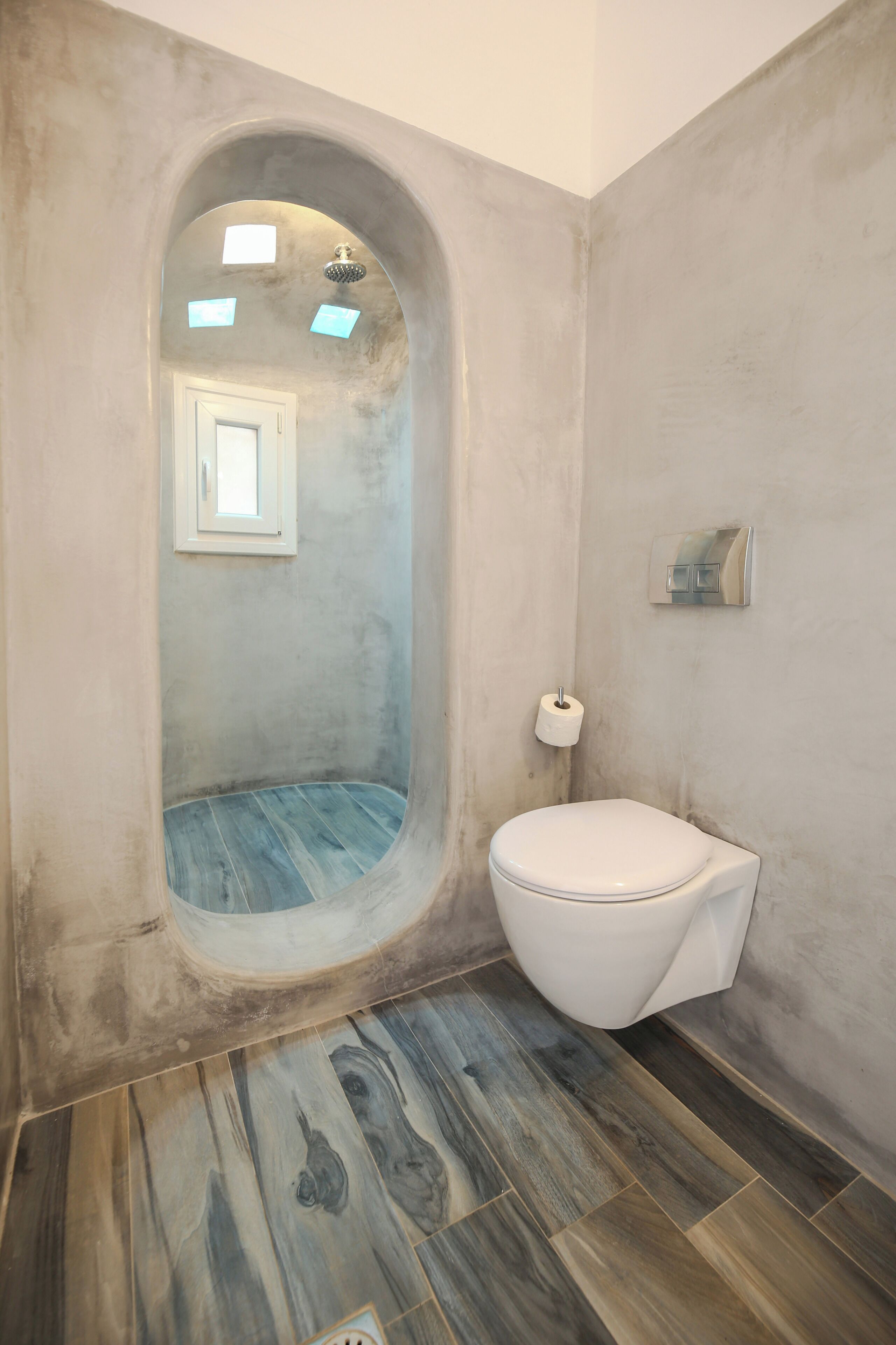 A bathroom with a built-in shower, a toilet, and a small window.
