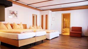 A bedroom with a large bed, a wooden floor, a red chair, and a bathroom visible through an open door. - Eigerblick (Grindelwald)