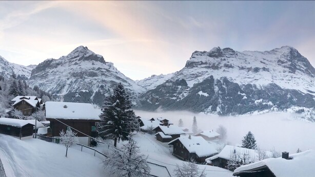 A snow-covered mountain village with traditional wooden houses and a view of towering peaks. - Eigerblick (Grindelwald)