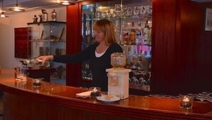 A bar area with a bartender, shelves with bottles, and a counter with glasses and a menu. - Eigerblick (Grindelwald)