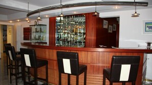 A bar area with a curved wooden counter, three bar stools, and a glass display case filled with bottles. - Eigerblick (Grindelwald)