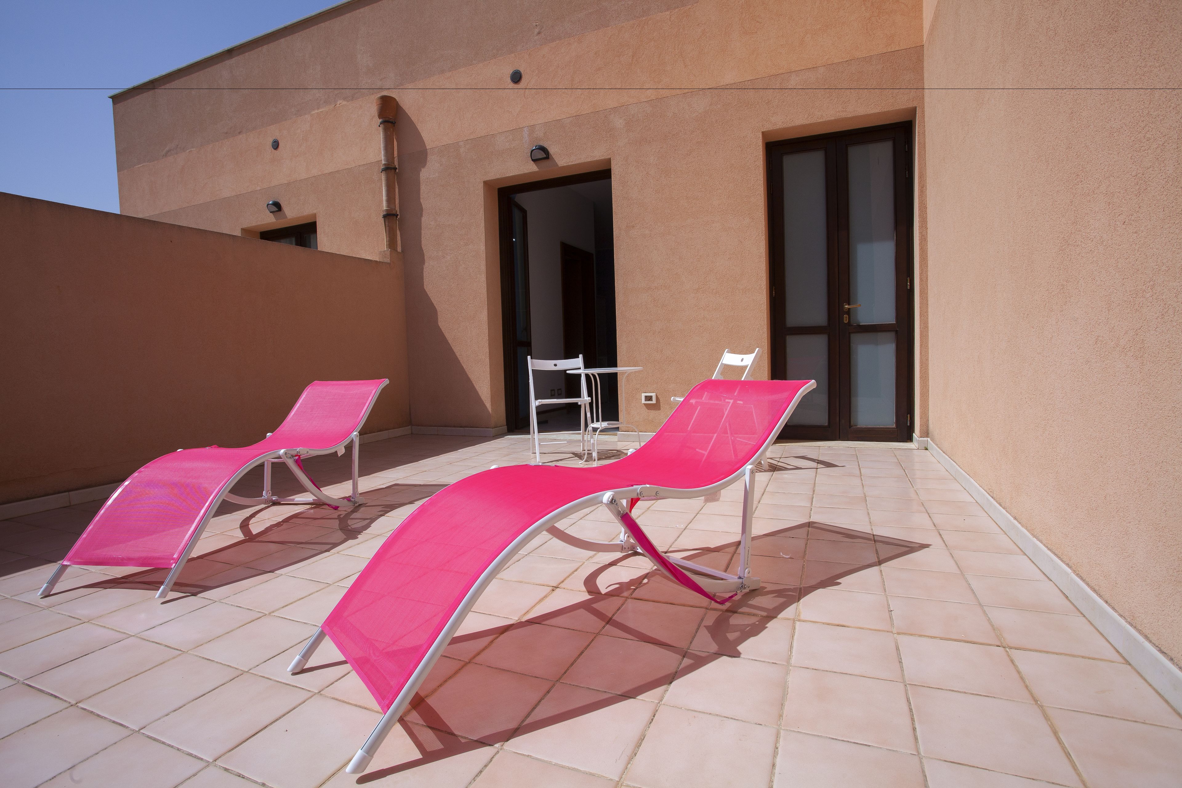 A balcony with two pink sun loungers and a small table.