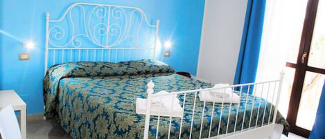 A bedroom with a blue wall, a white metal bed frame, a patterned bedspread, and a white chair.
