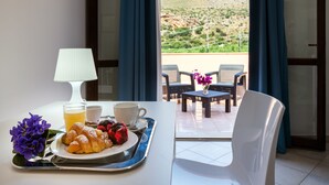 A breakfast tray with croissants, berries, and juice on a table with a lamp and a view of a balcony with chairs and a table. - Hotel Achibea (San Vito Lo Capo)