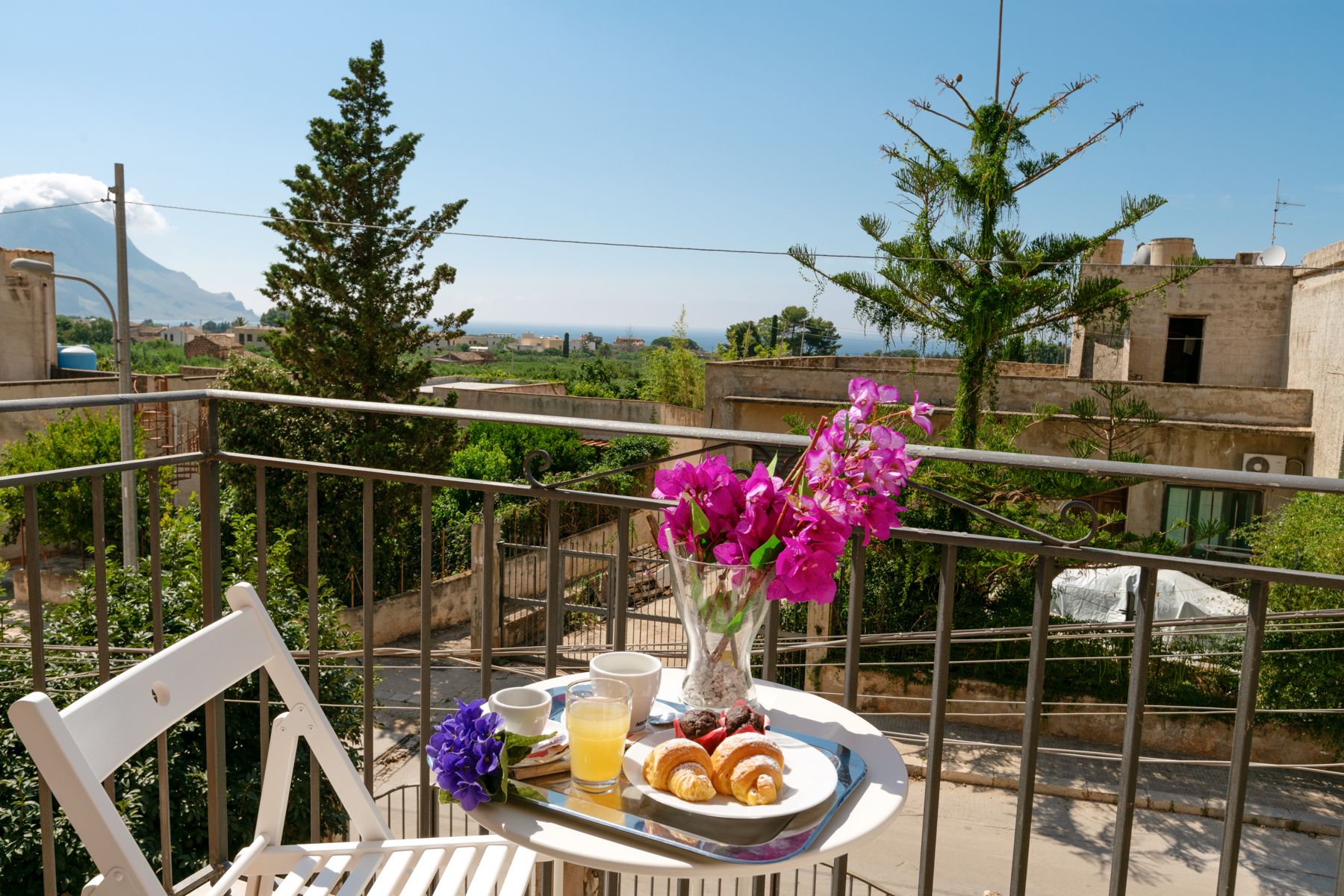Een balkon met een ontbijtje, compleet met croissants, een drankje en bloemen.