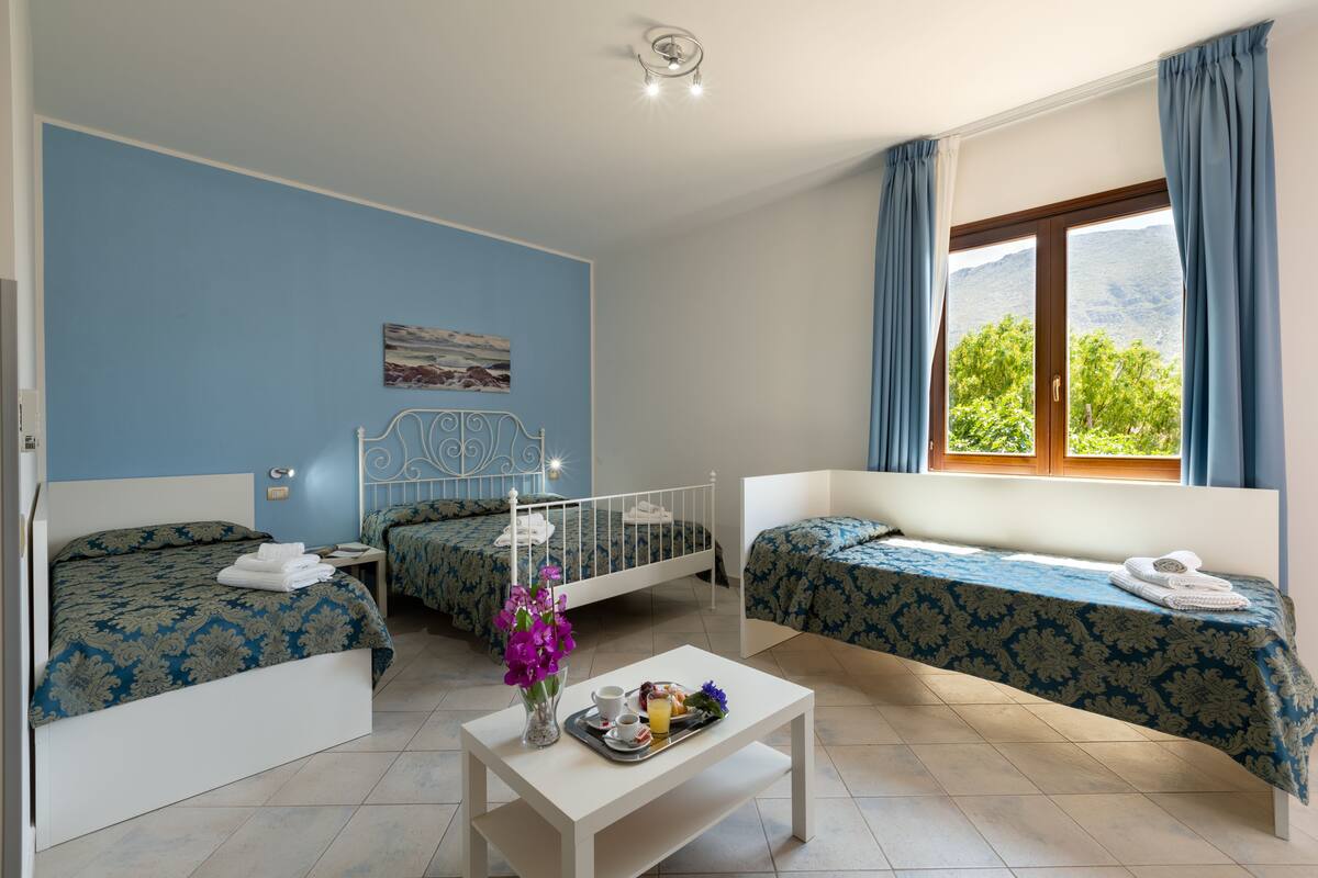 A hotel room with two beds, a dining table with breakfast, and a window with a mountain view.