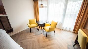 Una habitación de hotel con una cama, una mesa redonda con cuatro sillas amarillas y un ventanal con cortinas.