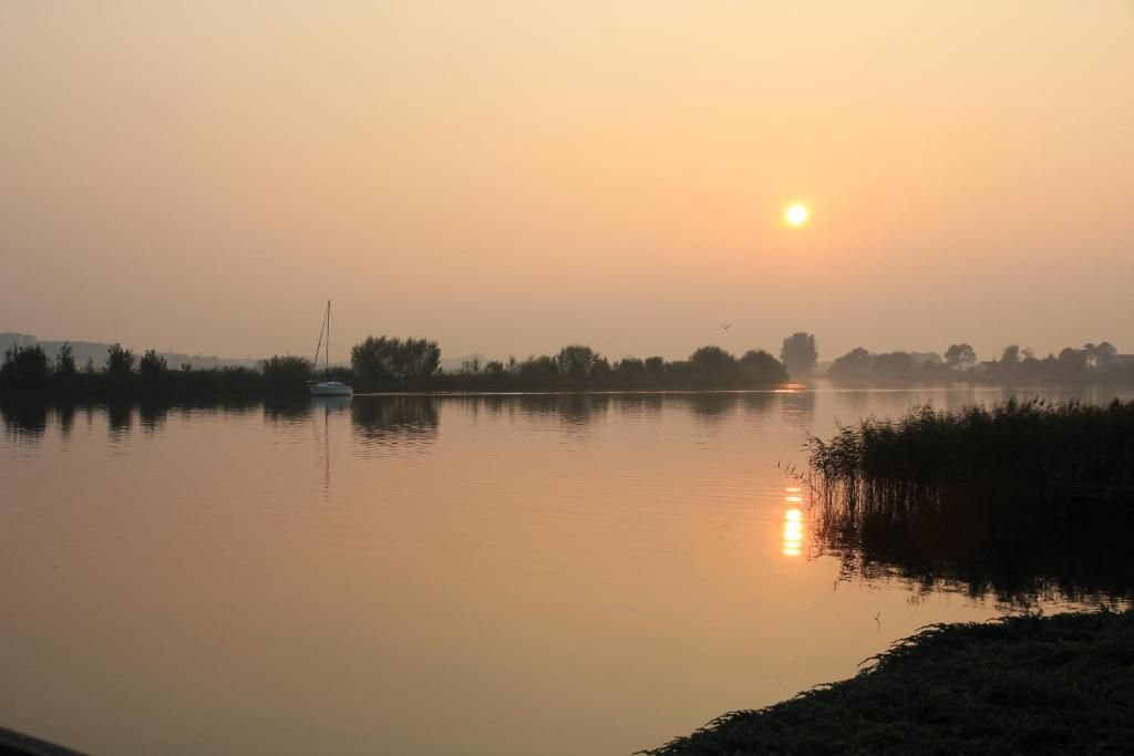 A calm lake at sunrise with a boat and distant trees.