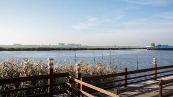 A wooden deck overlooking a calm river with distant buildings.
