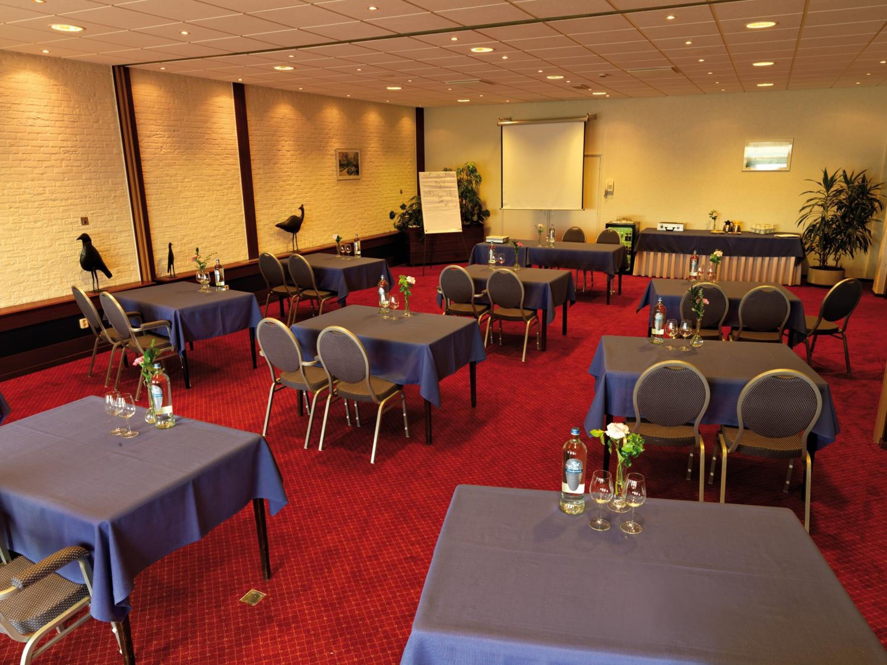 A conference room with multiple tables and chairs, a projector screen, and a whiteboard.
