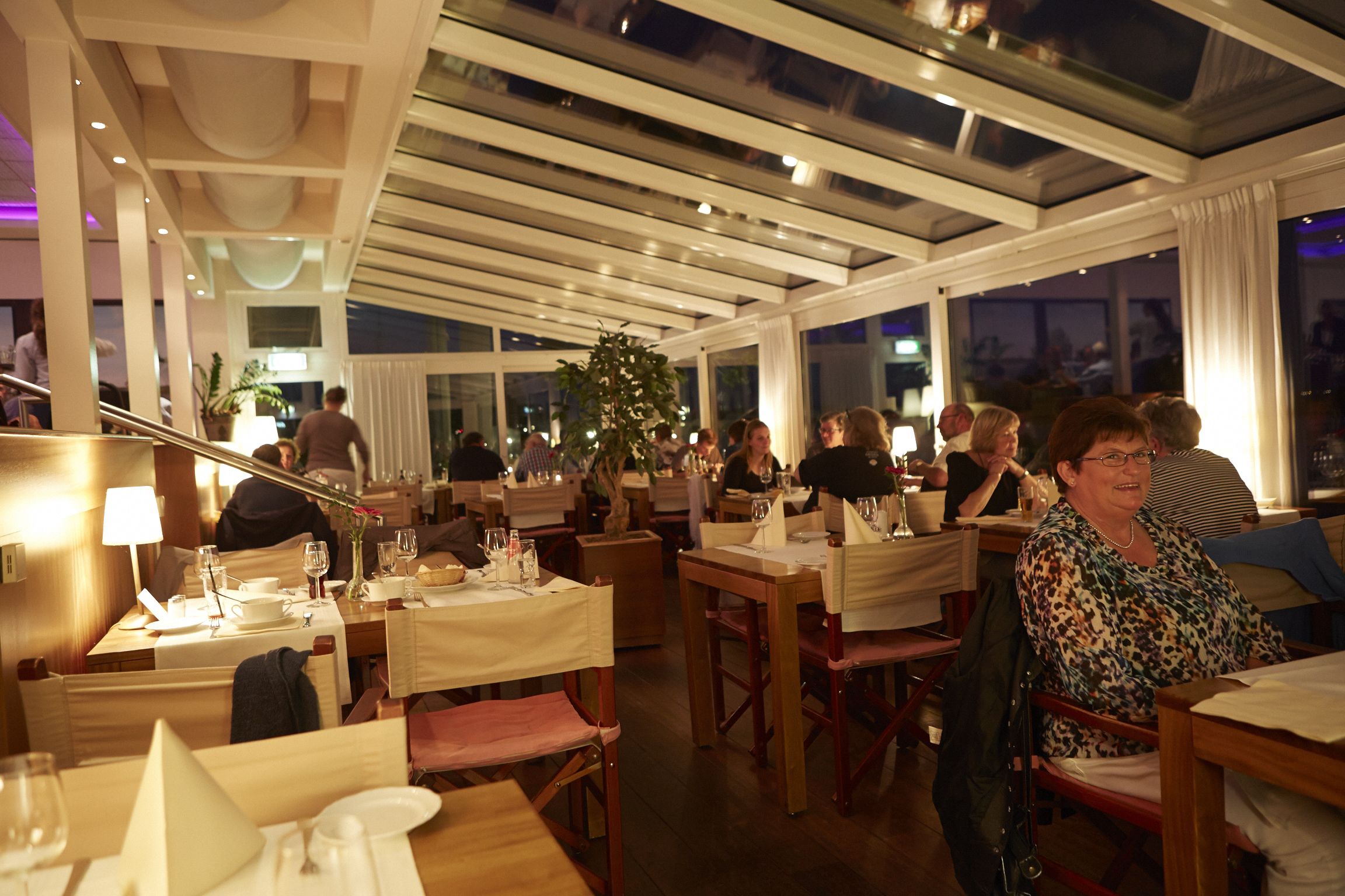 Restaurante com várias mesas, cadeiras e teto com claraboias.