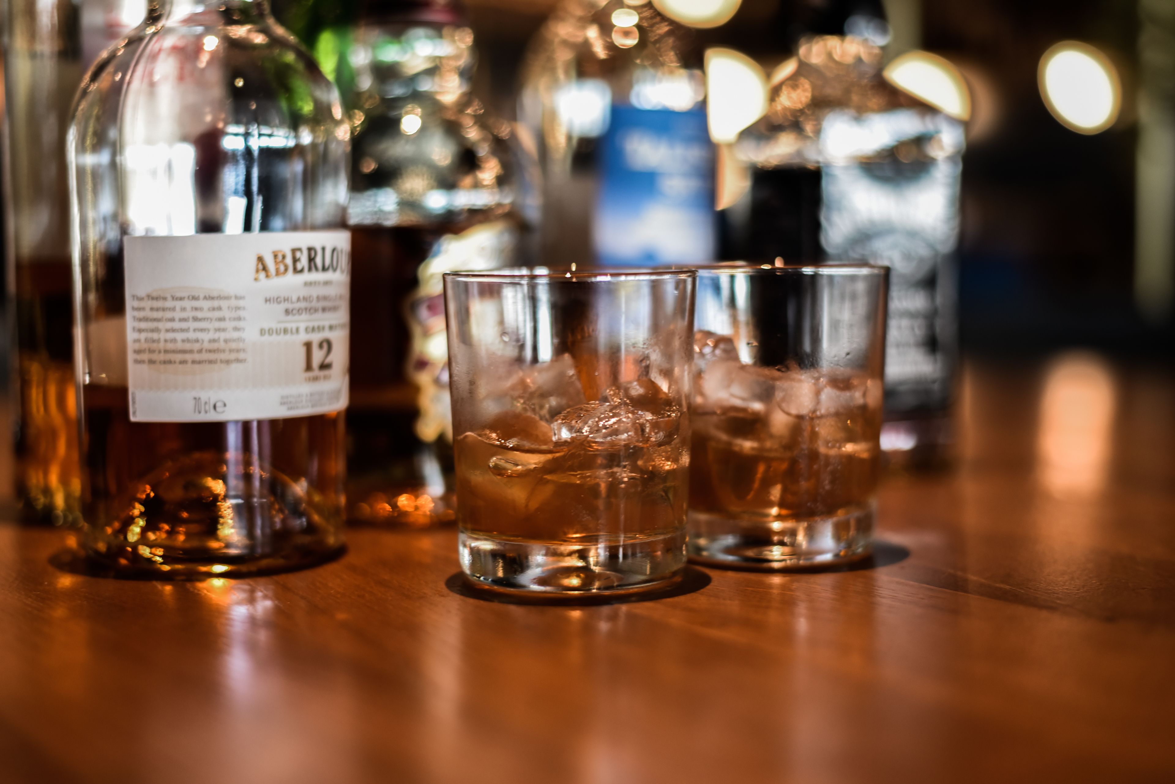Una botella de whisky Aberlour y dos vasos con hielo sobre una superficie de madera.