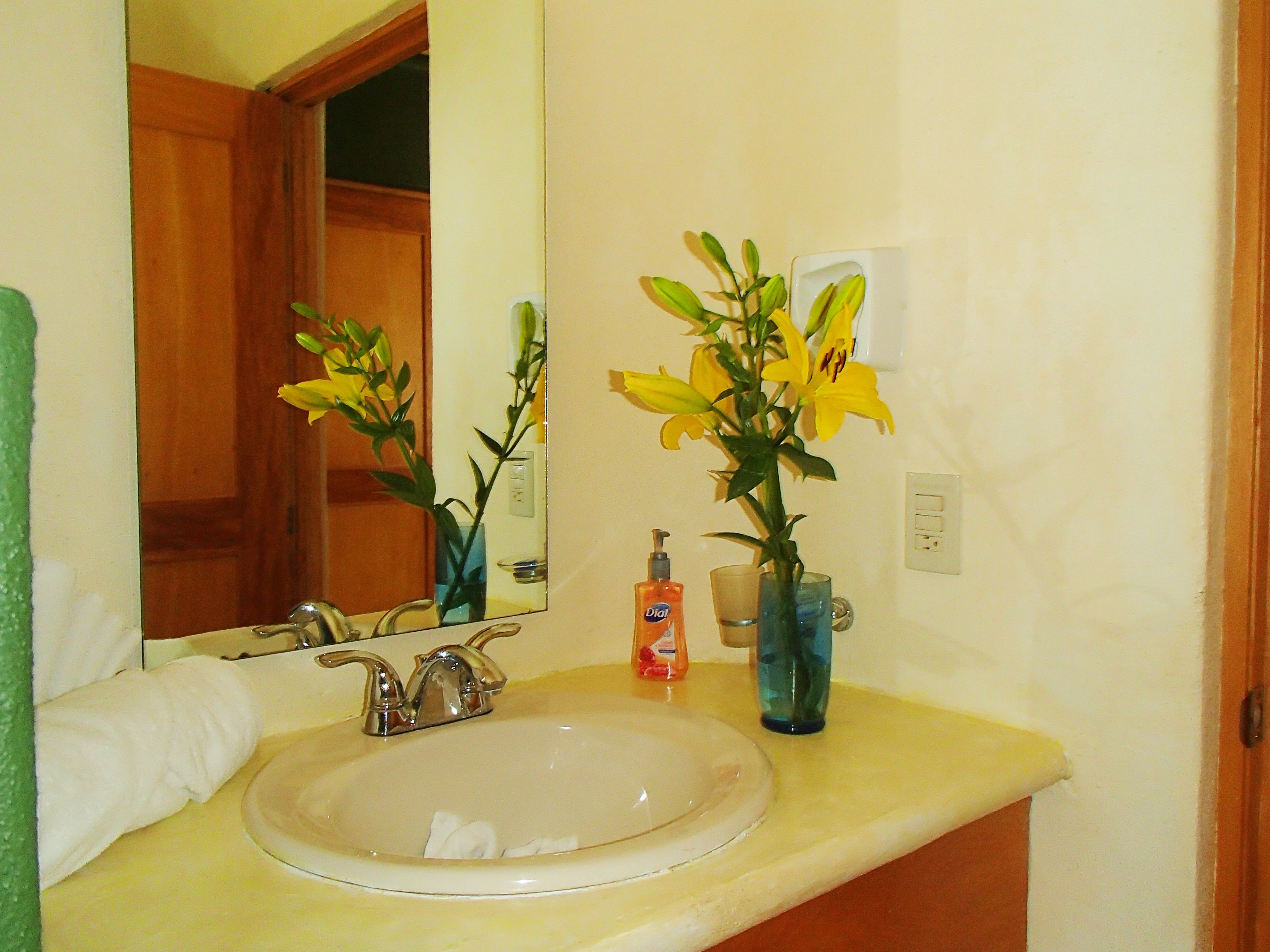 A bathroom with a sink, mirror, and two vases with flowers.
