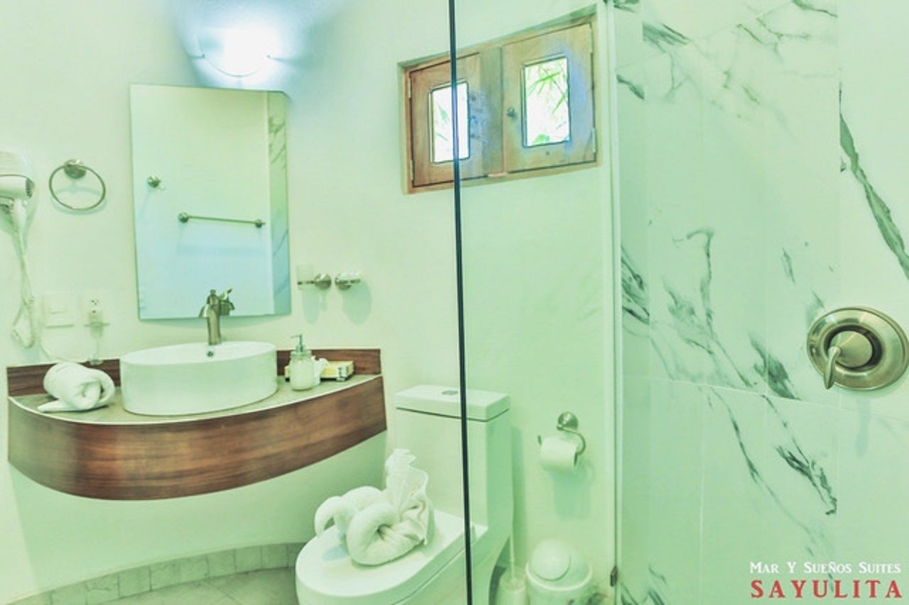 A bathroom with a wooden vanity, a white sink, a mirror, a toilet, and a glass shower enclosure.
