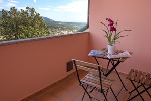 Varanda com vista para uma paisagem montanhosa, planta em vaso, jornal e cadeira de madeira.