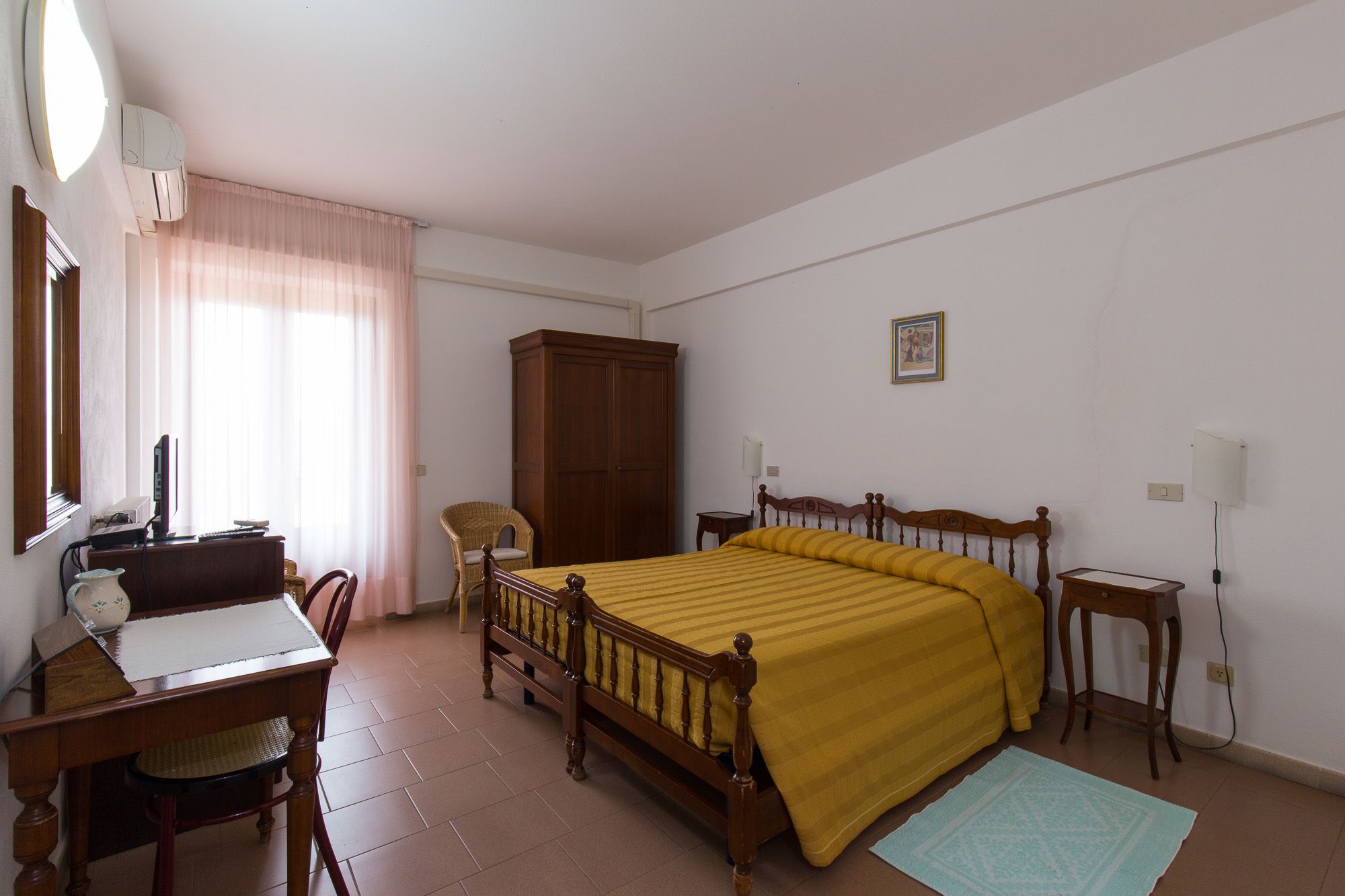 A bedroom with a wooden bed, a desk with a chair, a wardrobe, and a window with curtains.