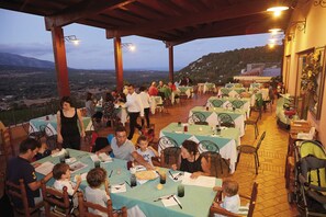 Restaurante ao ar livre com mesas e cadeiras, com uma paisagem deslumbrante ao fundo.