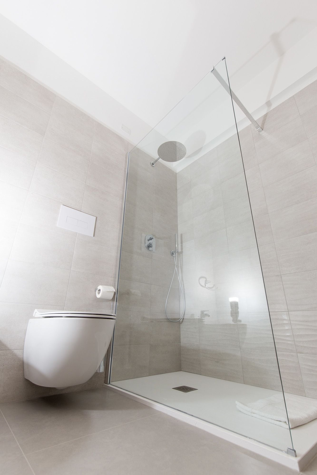 Een moderne badkamer met een glazen douchecabine, een toilet en een wandbevestigde handdoekhouder.