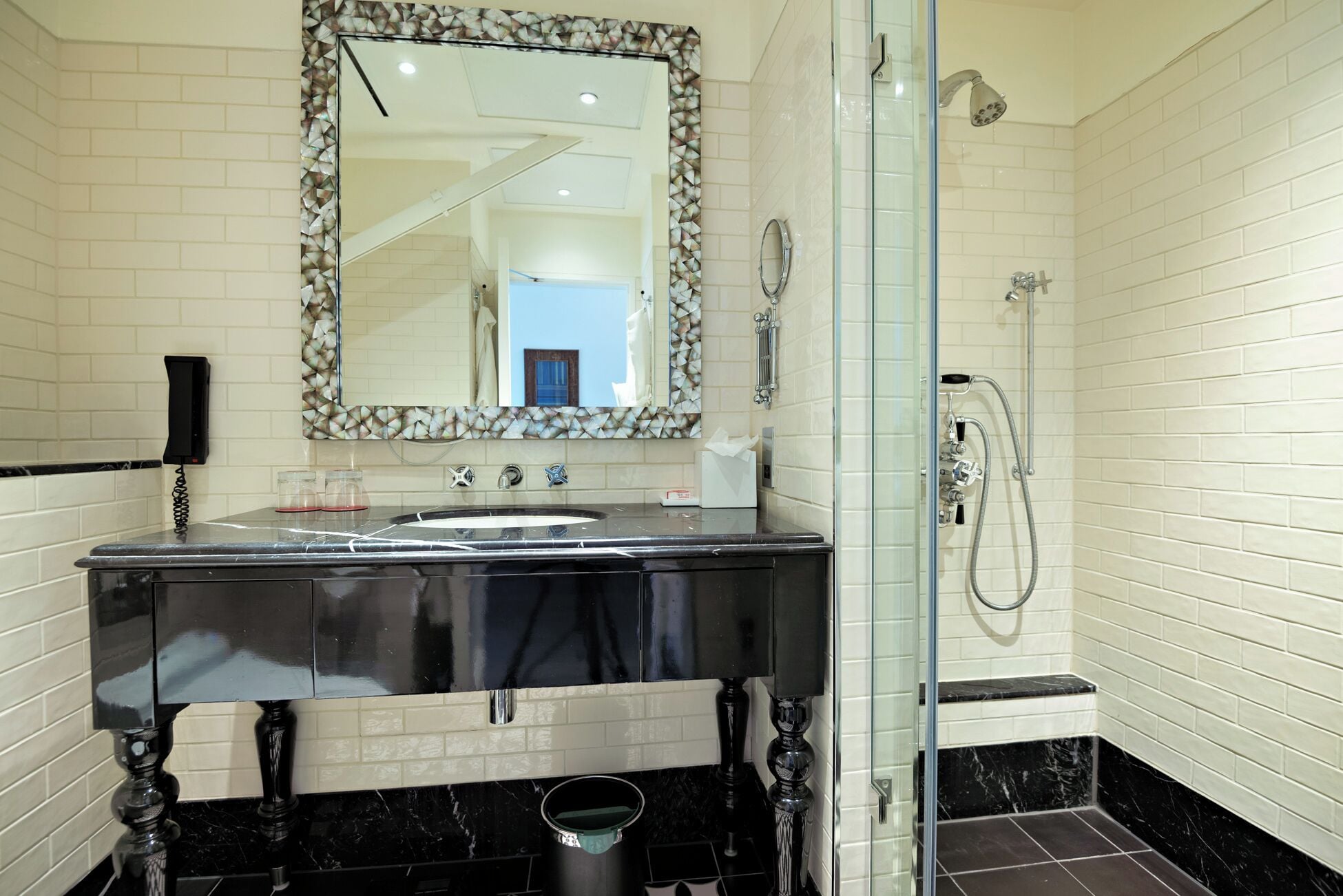 Een moderne badkamer met een zwart marmeren wastafel, een douche met glazen wanden en een decoratieve spiegel met een geometrisch lijstwerk.