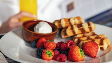 Ein Teller mit Waffeln, Erdbeeren, Blaubeeren, Himbeeren und einer Schüssel Joghurt.
