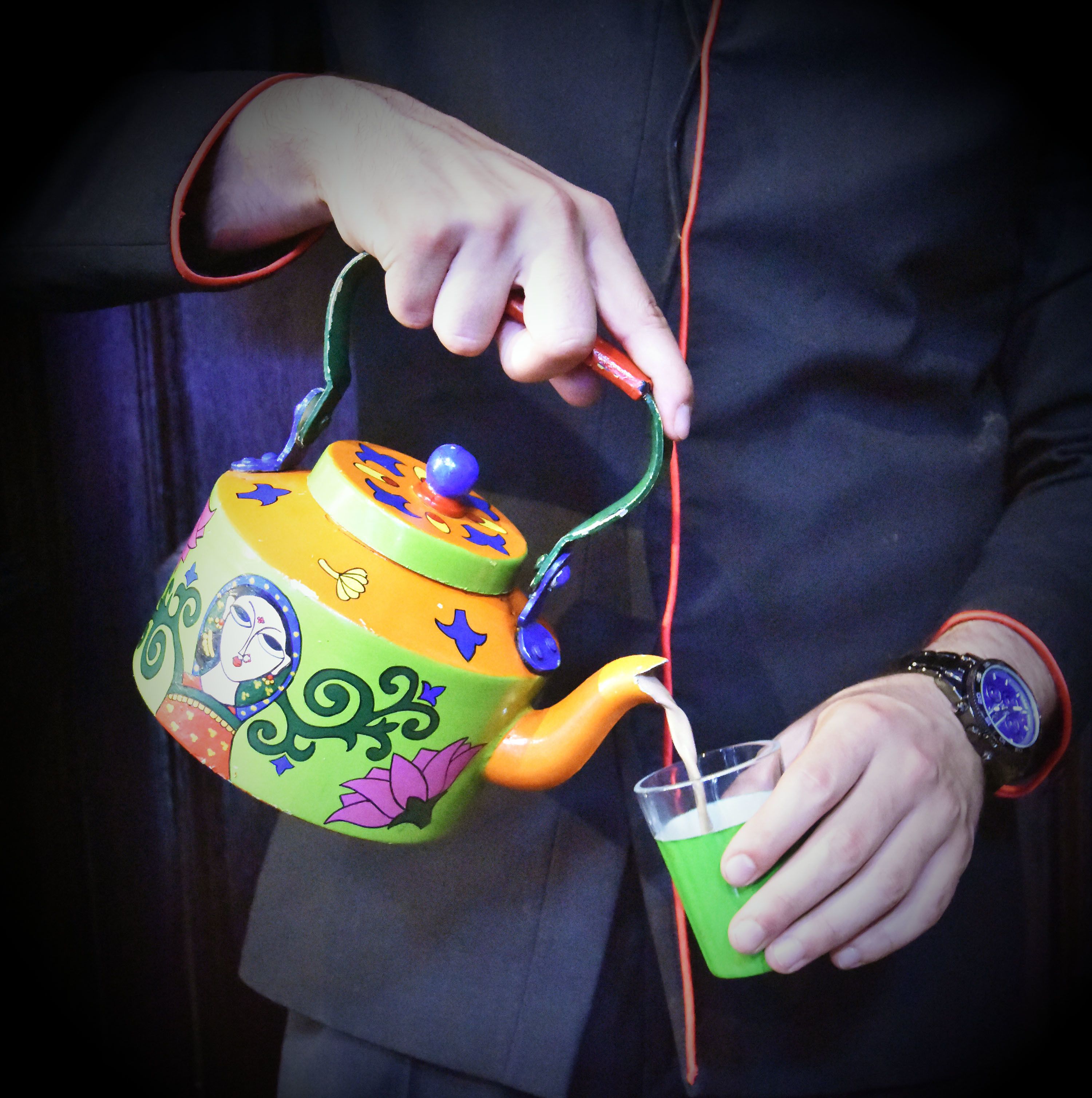 Eine Person hält eine bunte Teekanne und gießt Flüssigkeit in eine Tasse.
